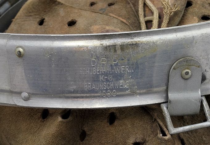 Markings on an aluminum liner dated 1938. «D.R.P.» means Deutsche Reichs Patent and the manufacturer is Schuberth-Werk K.-G. in Braunschweig. The abbreviation K.G. stands for Kommanditgesellschaft which means Ltd. or Limited. Notice to the left the 2 small aluminum rivets to which the reinforcing plate is attached and to the right the chinstrap bale with square corners.