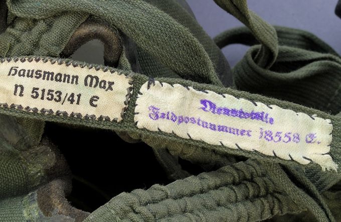 Naming on cloth line on a gas mask used by a German navy soldier. Dienststelle (serving location) and Feldpostnummer 18558 Stab (staff) und Einheit Marine-Flak Abteilung 814 Denmark/Norway. The other cloth tag says; 