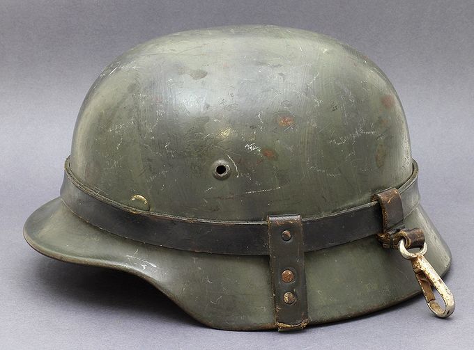 M35 Q64 with hand brushed darker green in patterns on top of the factory paint. The helmet has the carrying leather strap. The helmet with the strap hook was normally attached the soldiers field equipment when they were on the march (another Norwegian collection).